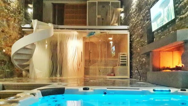 A modern indoor pool area with a spiral staircase, a fireplace, and a stone wall backdrop.