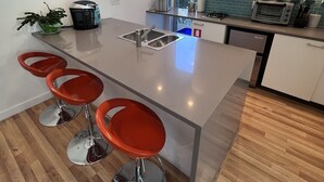 A modern kitchen with a central island, stainless steel appliances, and red bar stools. - Stunning Stono River Guesthouse w/ Scenic Water Views &  Pool (Charleston)