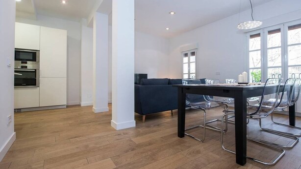 A modern kitchen with built-in appliances, a dining area with a table and chairs, and a sofa in a bright room with large windows. - Bright apartment T3 (Tours)