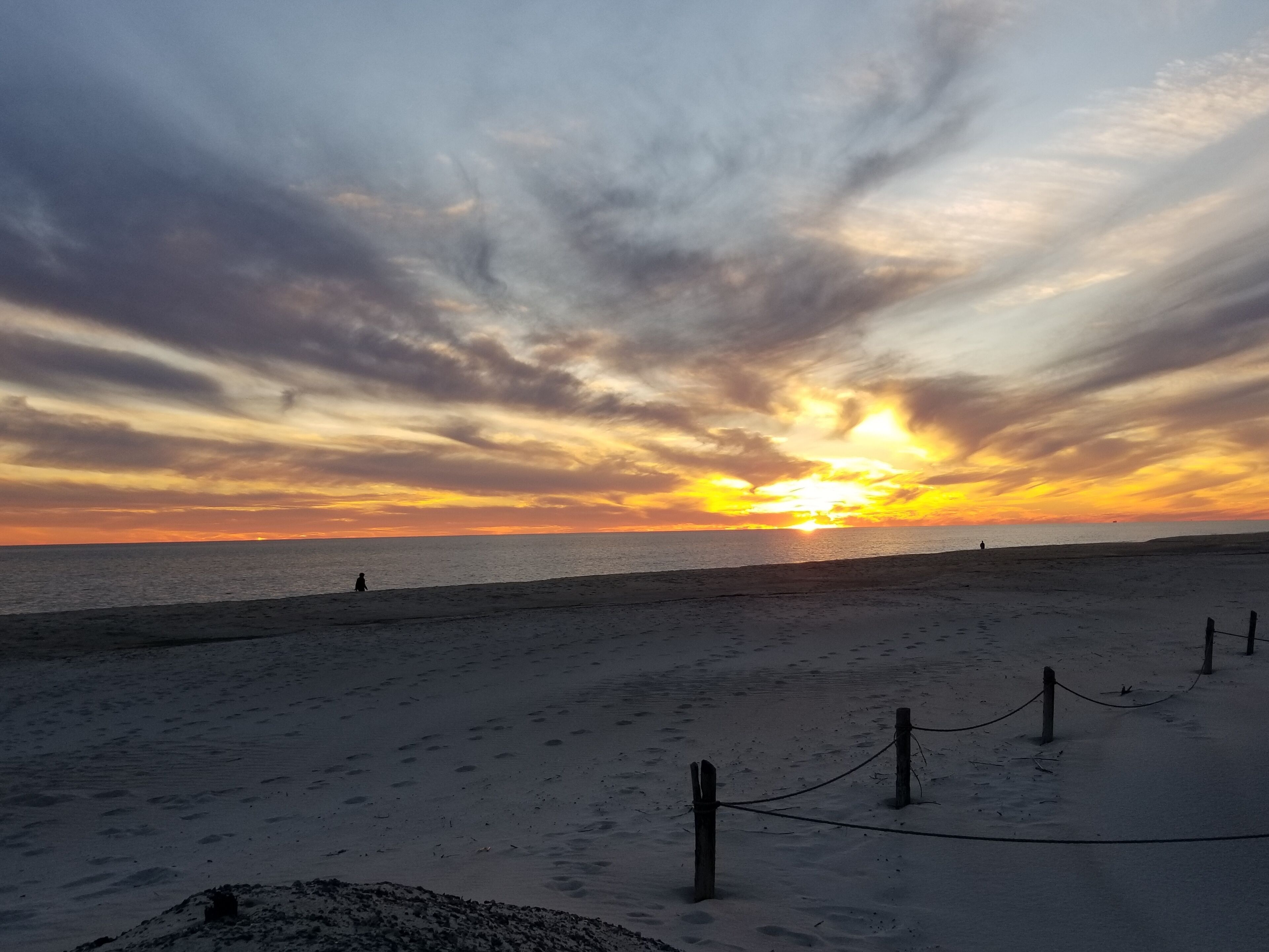 A beach with a sunset, sandy shore, and a rope barrier.