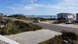 Una carretera costera con dos coches blancos estacionados al lado, un muelle al fondo y una casa de playa con un letrero.