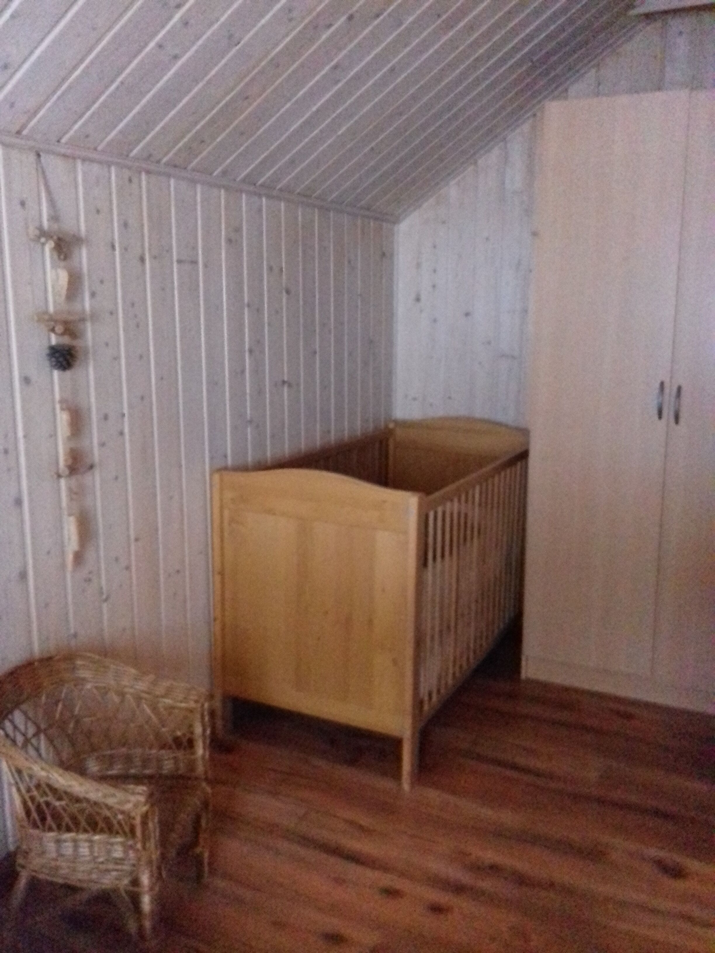 Et værelse med trægulv, en trækæbe, en fletstol og en hvid garderobe.