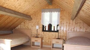 A wooden-paneled attic bedroom with two beds, a window with a white curtain, and bedside lamps. - Adddddddddddd (La Bresse)