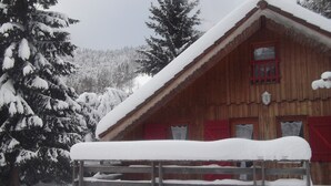 A wooden cabin with a snow-covered roof and windows, surrounded by snow-laden trees. - Adddddddddddd (La Bresse)