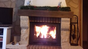A stone fireplace with a brick surround, a mounted television above it, and a Christmas tree on top. - Adddddddddddd (La Bresse)