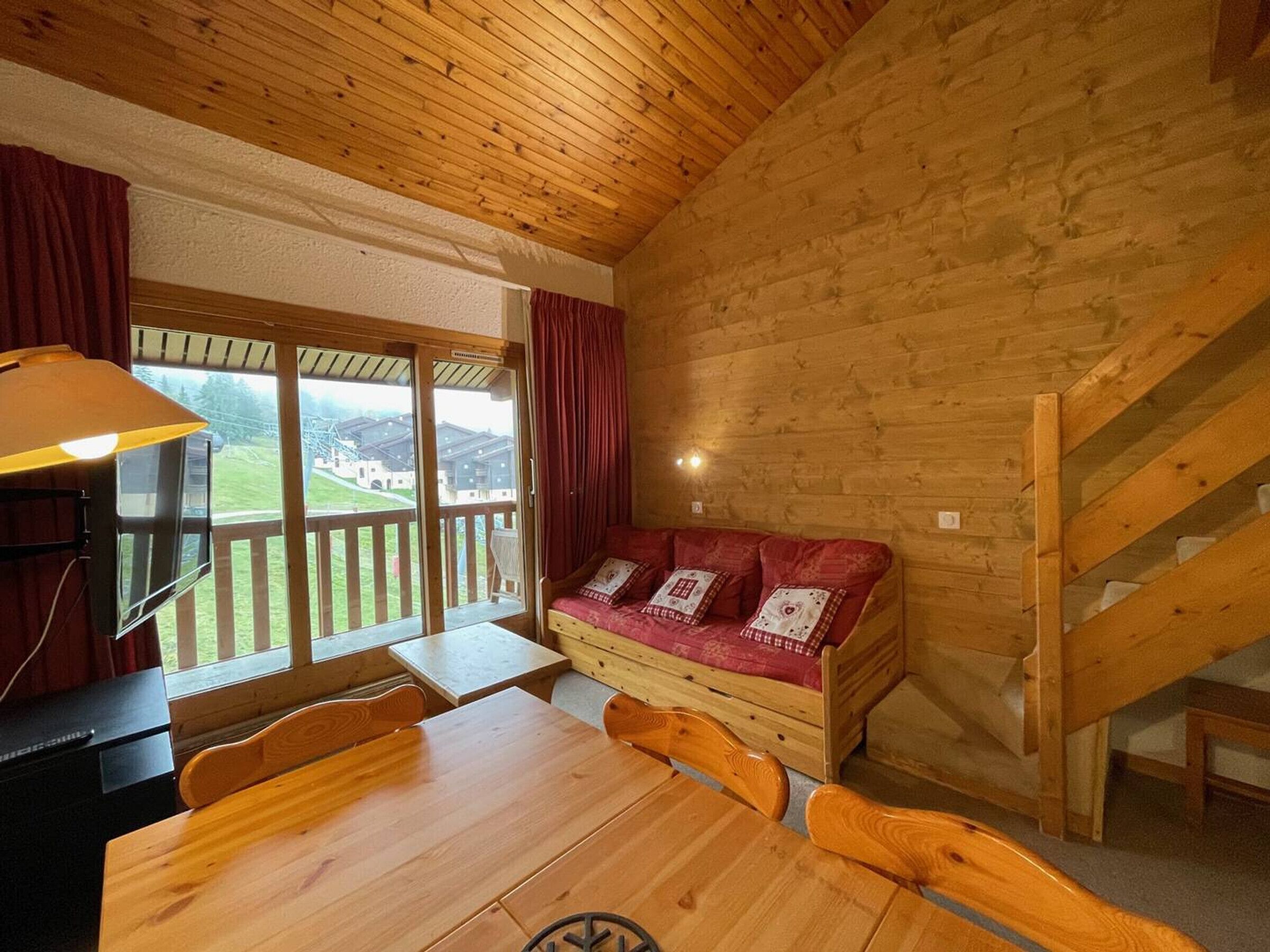 L'intérieur d'un chalet en bois comprend une table à manger, des chaises en bois, un canapé avec des coussins, un téléviseur et un escalier.