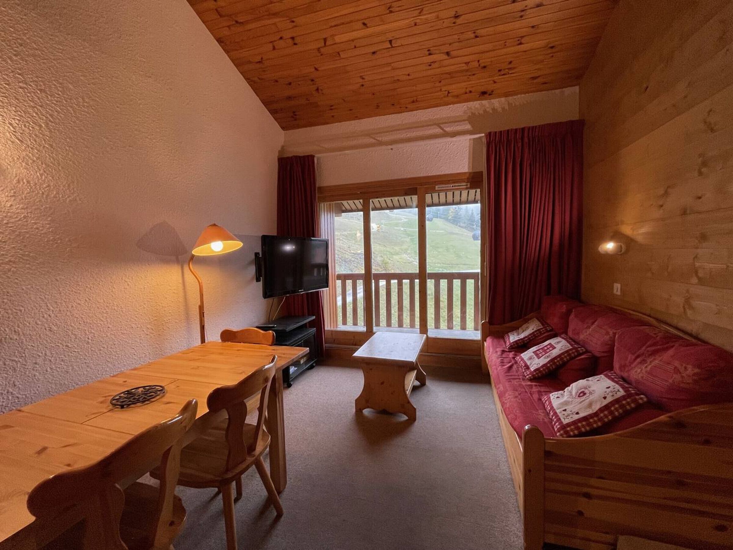 A cozy room with a wooden table, chairs, a sofa, a TV, and a window with curtains.