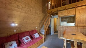 Et hyggeligt interiør i en hytte med en trappe i træ, en rød sofa med mønstrede puder, et træbord og et køkken.