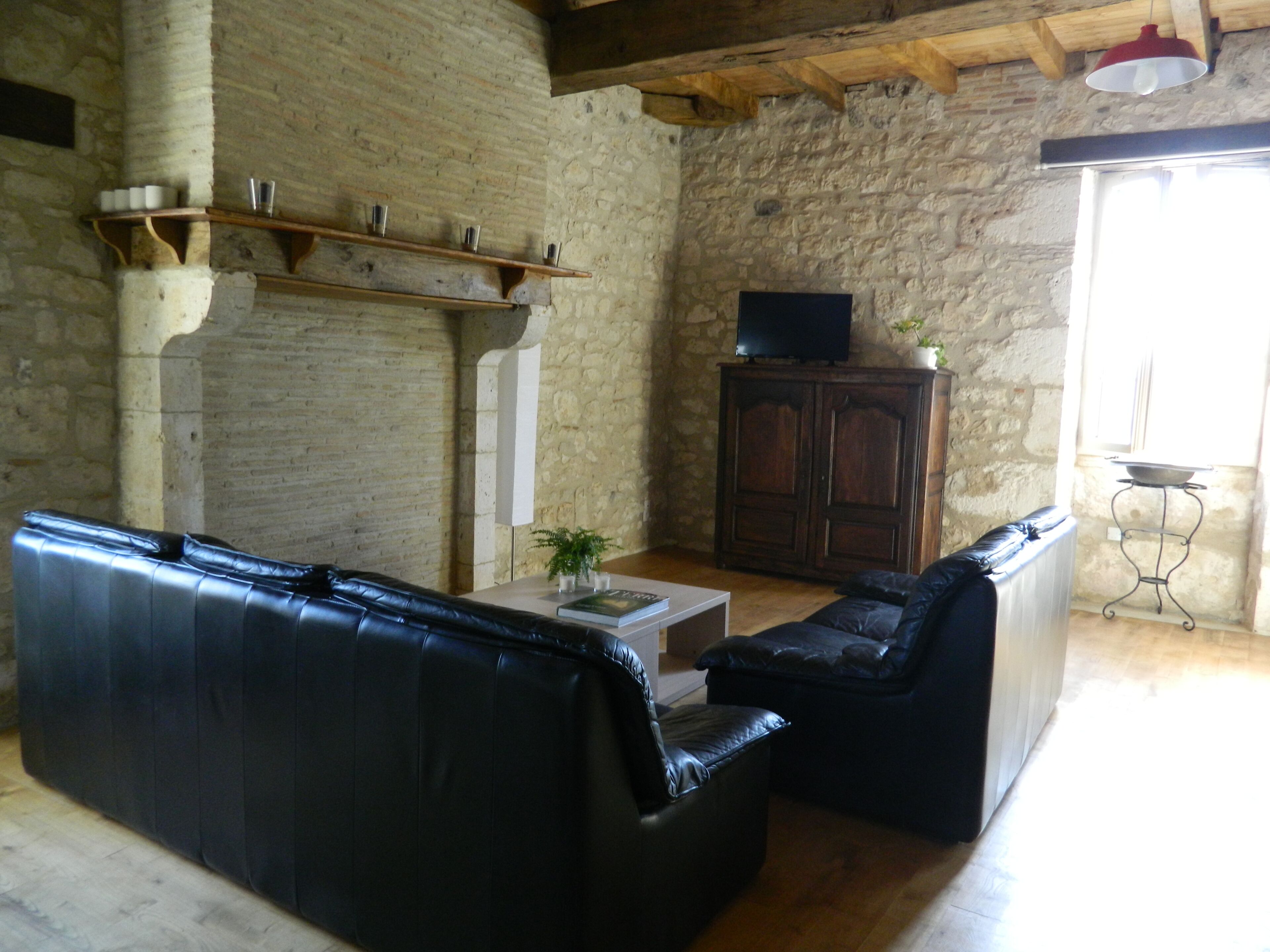 A living room with a stone wall, a fireplace, a television on a cabinet, and a black leather sofa.