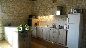 Une cuisine avec des murs en pierre, des armoires en bois, un four encastré, un four à micro-ondes, un réfrigérateur et une plante.