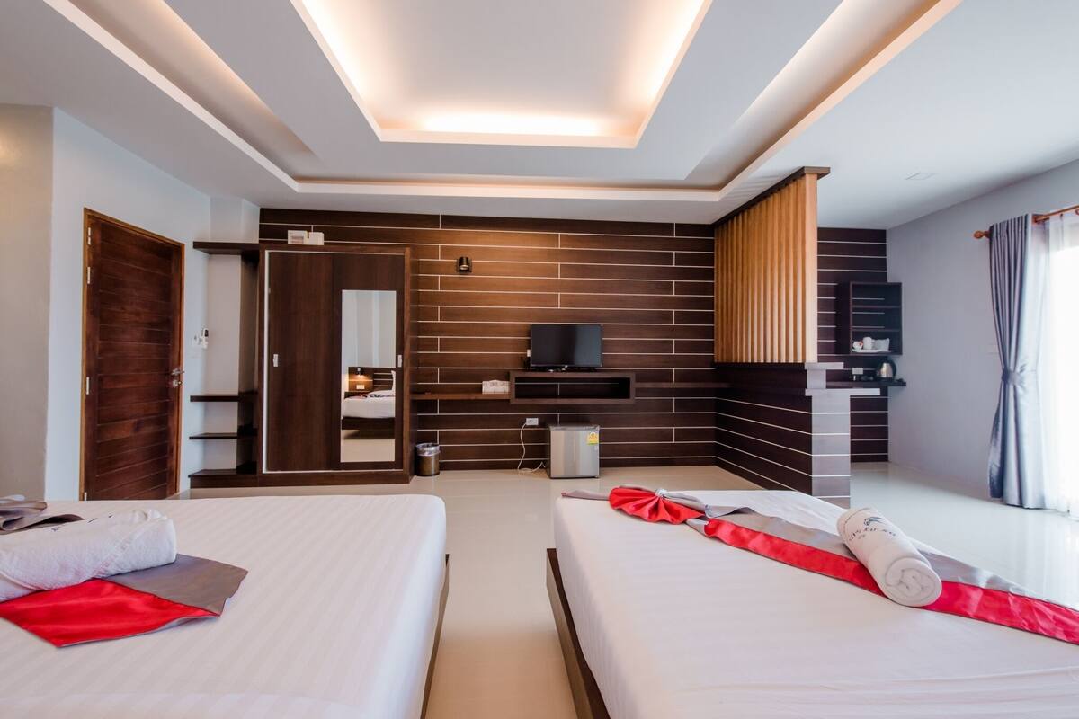 A hotel room with two beds, a TV, a mirror, a wardrobe, and a ceiling light.
