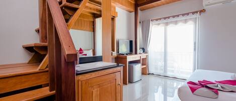 A wooden staircase leading to a balcony, a bed with a white and pink blanket, a desk with a computer, and a television.