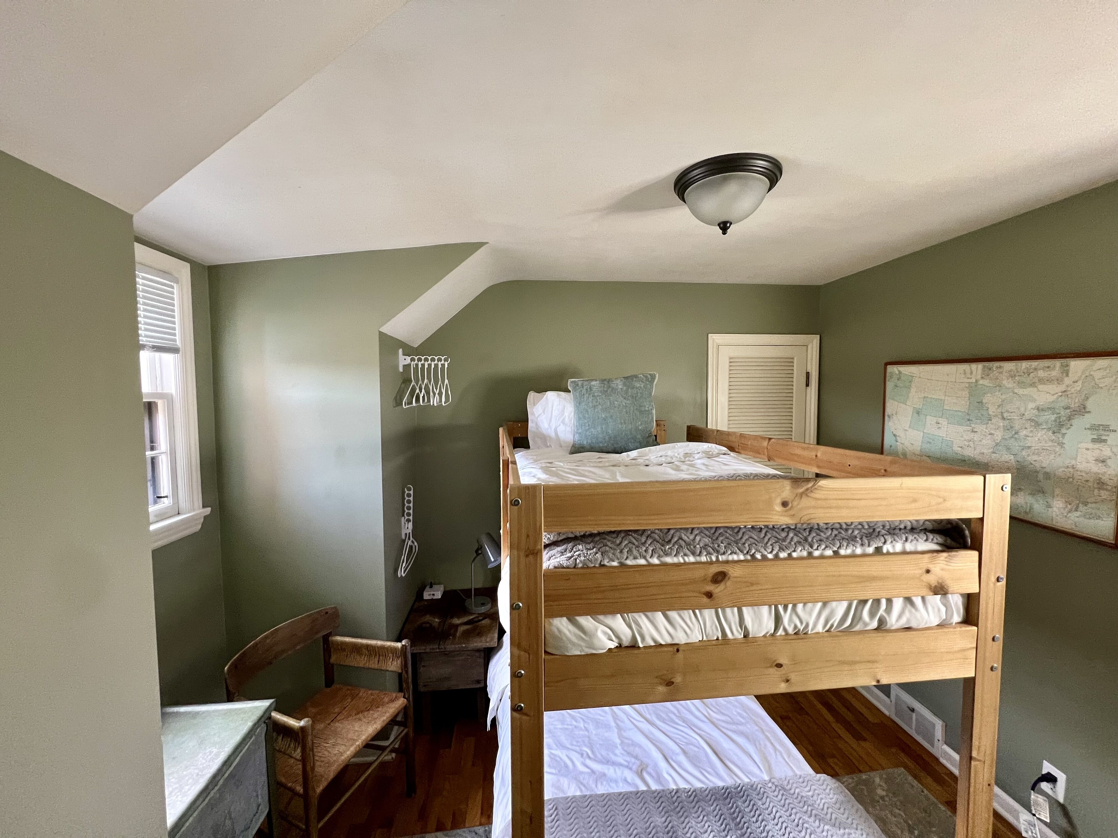 A bunk bed room with a desk, chair, and a map on the wall.