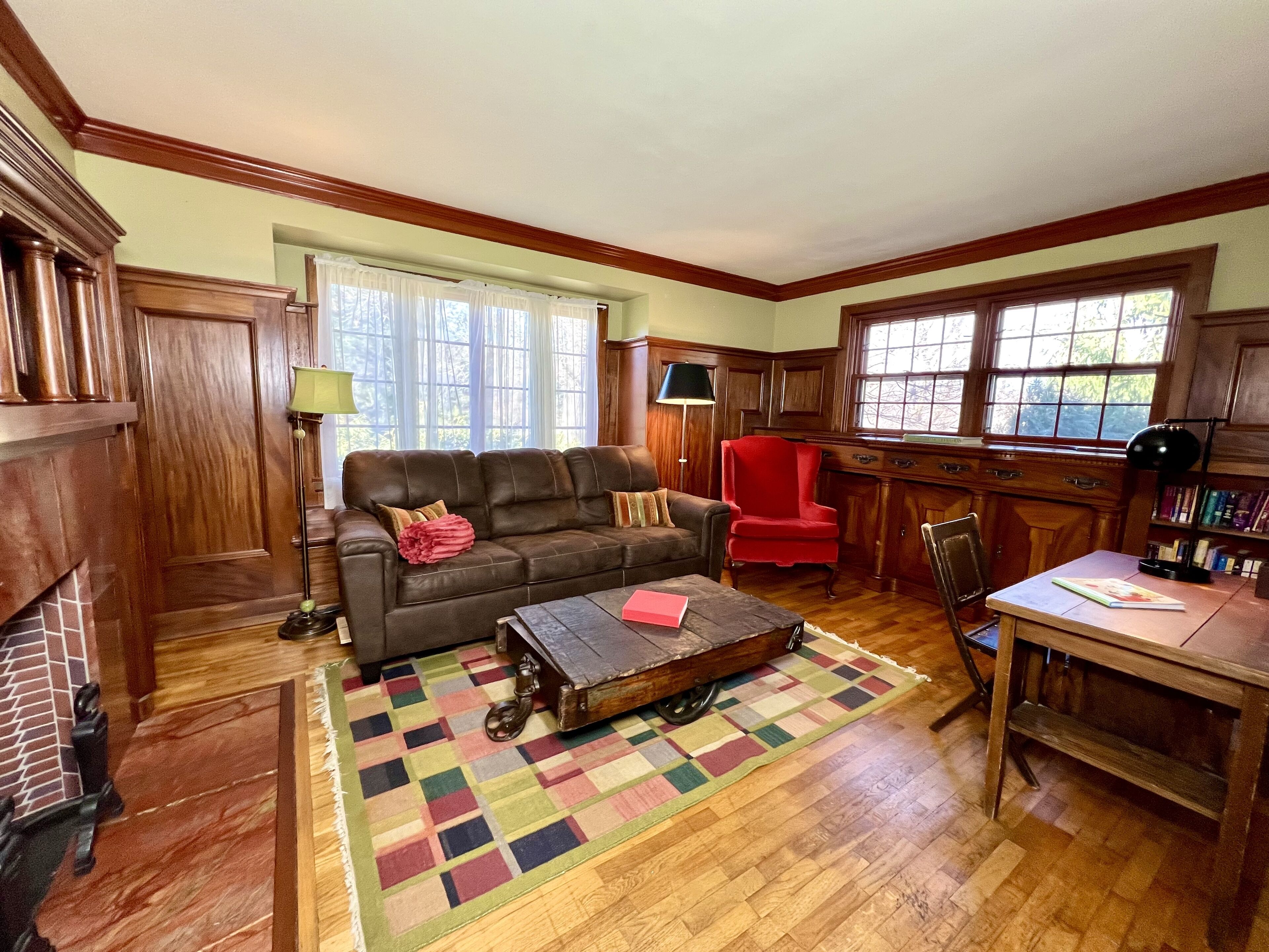 A cozy living room with a brown leather sofa, a red chair, a wooden coffee table, and a bookshelf.