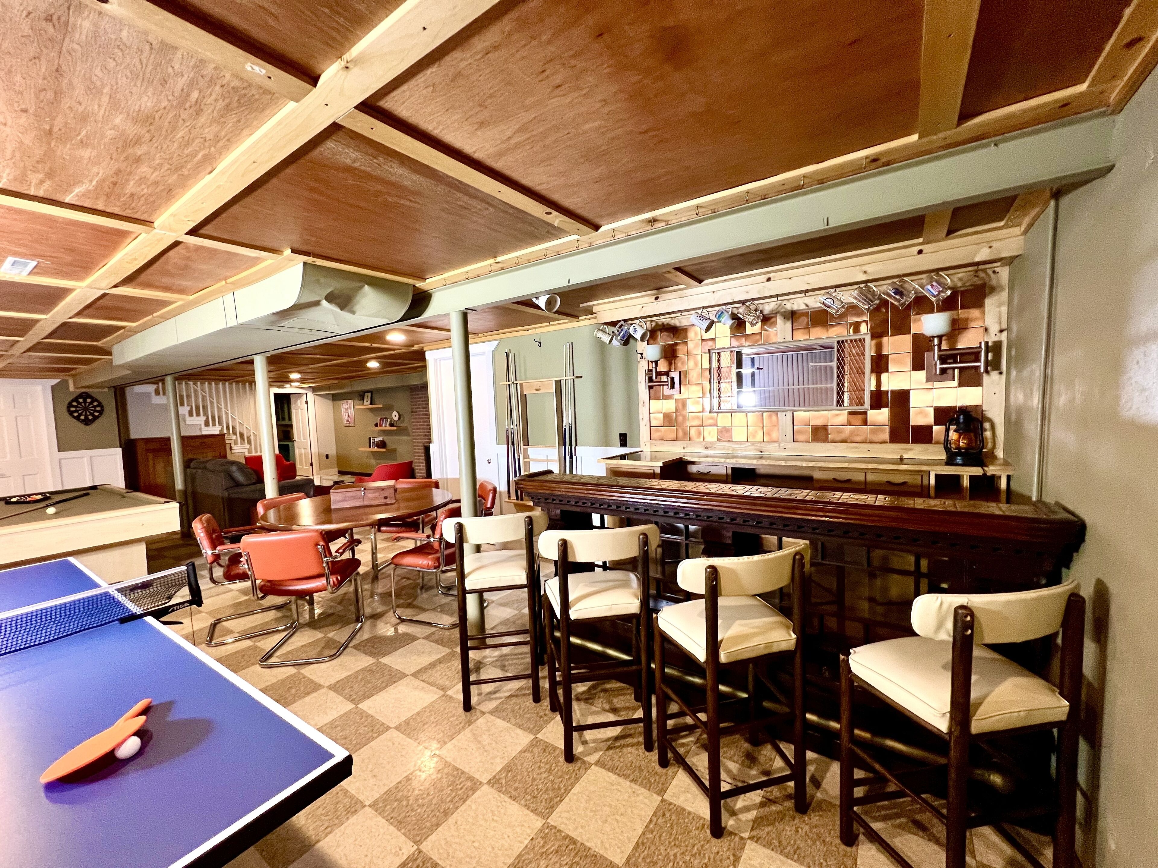 A room with a pool table, ping pong table, and bar area with stools.