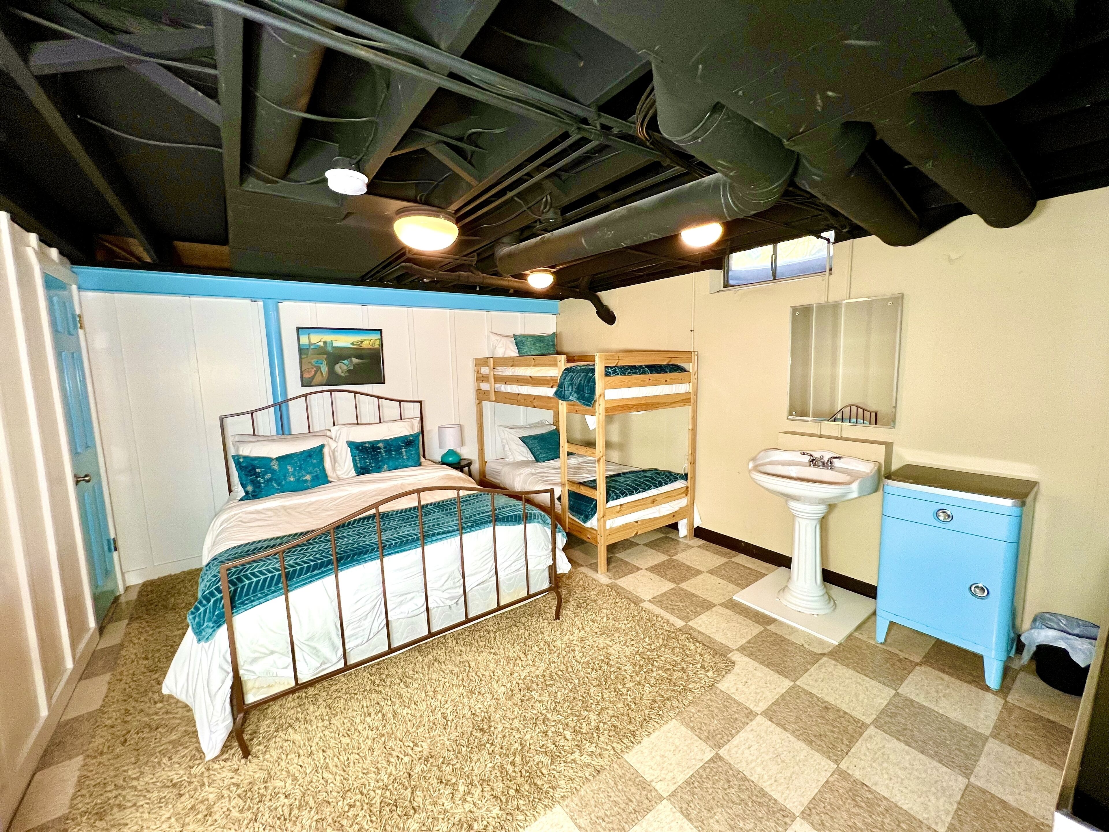 A room with a bunk bed, a single bed, a sink, and a mirror.