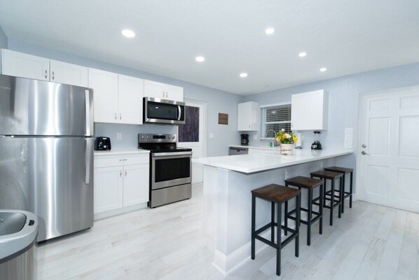 A modern kitchen with white cabinets, stainless steel appliances, and a central island with stools. - Cozy Pet Friendly Condo w/ Pool a Block from Siesta Village, 3 Blocks from Beach (Sarasota)