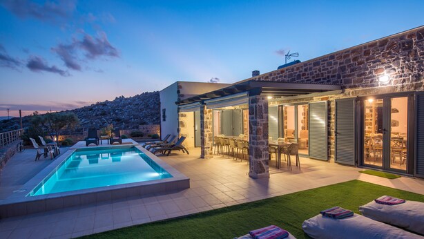 A modern outdoor pool area with a stone building, lounge chairs, and a dining area. - Mandy Luxury Villa by Cretevasion (Kokkini Hani)