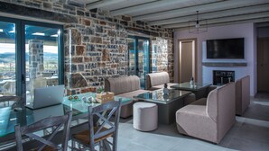 A modern living room with stone walls, a glass table, and comfortable seating. - Mandy Luxury Villa by Cretevasion (Kokkini Hani)