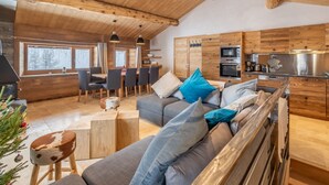 Un interior de cabaña moderno con comedor, sofá con cojines, un taburete de madera y una kitchenette.