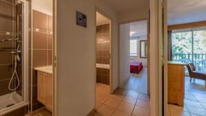 Un pasillo que conduce a un baño con ducha y lavabo, y vistas a un balcón con mobiliario exterior.