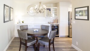 A dining area with a round table, four upholstered chairs, a chandelier, and a kitchen in the background. - Modern top floor corner unit with pool view  (Scottsdale)
