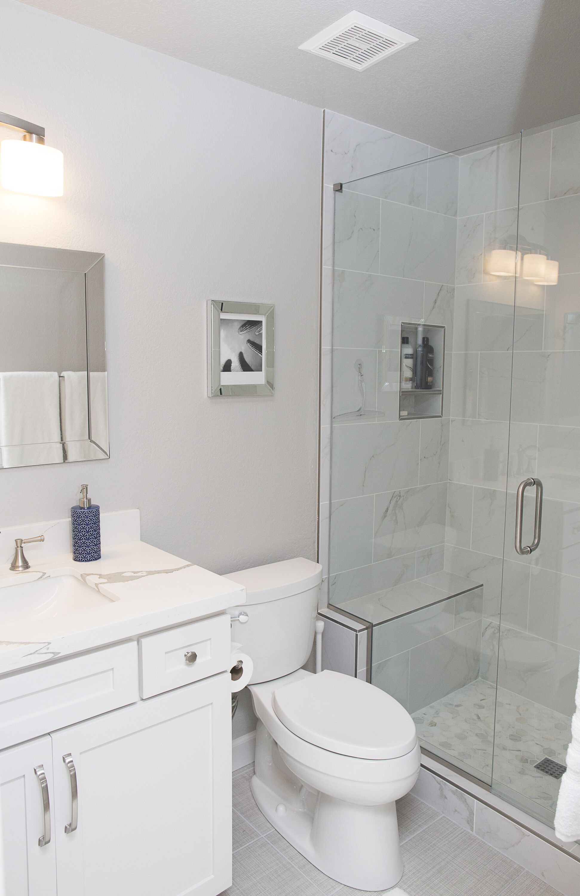 A modern bathroom with a glass-enclosed shower, a white toilet, and a vanity with a mirror and a soap dispenser.