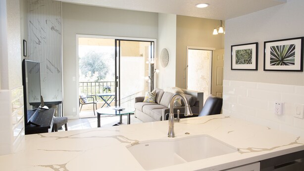 A modern kitchen with a large island, a built-in sink, and a dining area with a glass table and chairs. - Modern top floor corner unit with pool view  (Scottsdale)