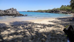 Ein Strand mit klarem, blauem Wasser, sandigem Ufer und Felsformationen.