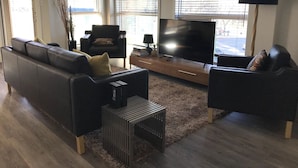 A living room with a black leather sofa, a black armchair, a TV, and a lamp.