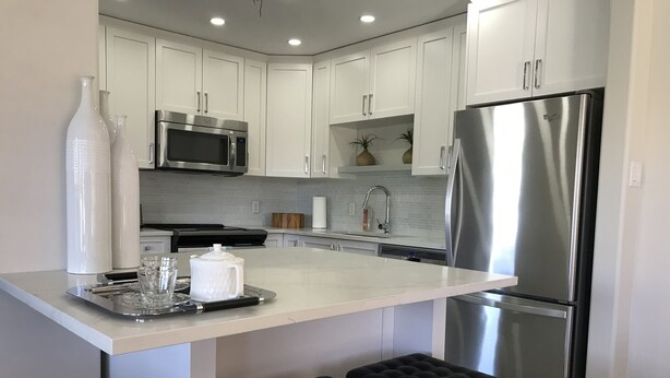 A modern kitchen with white cabinetry, stainless steel appliances, and a central island with stools.