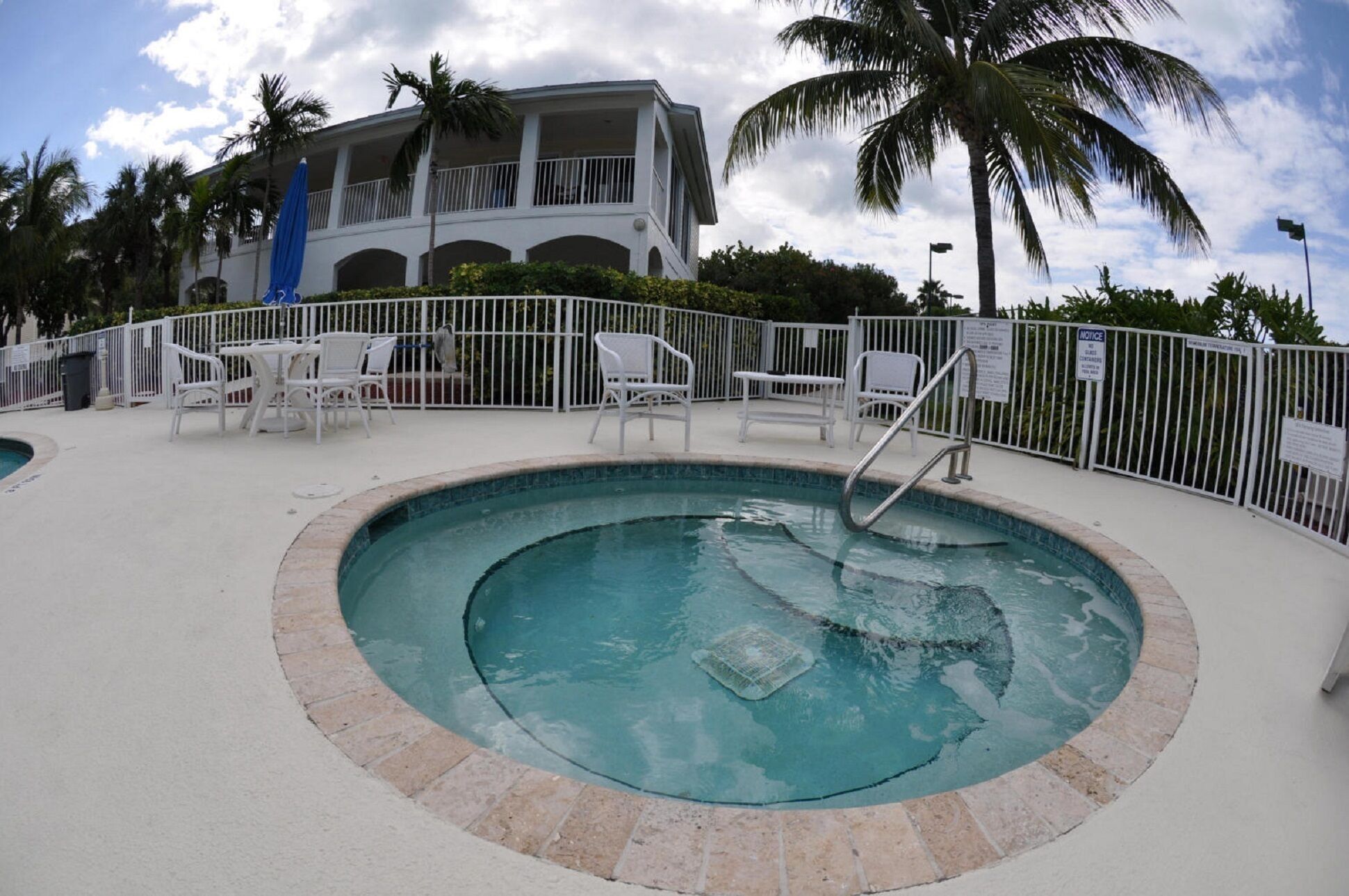 A swimming pool with a metal ladder, surrounded by a white fence and white chairs.