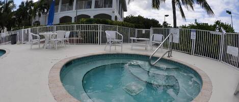 A swimming pool with a metal ladder, surrounded by a white fence and white chairs.
