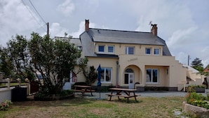 A two-story building with a beige facade, a covered patio area, and a visible entrance. - villa for 10 people (Bréhal)