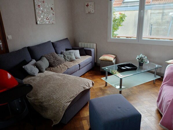 En stue med sofa, skammel, sofabord i glas og en rød lænestol.