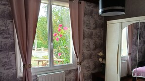 A bedroom with a bed, a window with curtains, a radiator, and a wardrobe. - villa for 10 people (Bréhal)