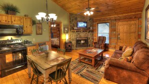 A cozy cabin interior with a stone fireplace, wooden ceiling, and a dining area with a table and chairs. - Nature's Harmony #10 Cabin – Your Perfect Getaway (Sevierville)