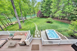 A deck with outdoor seating and a hot tub, surrounded by a well-maintained lawn and trees. - Private Coveside Paradise! WiFi, Hot Tub, FLAT Lot, Game Room, Kayaks, Beach (Huddleston)