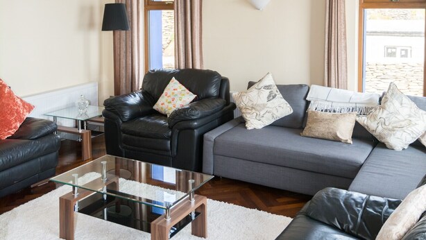 A spacious living room with a leather sofa, a glass coffee table, and a hanging light fixture.