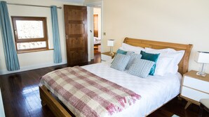 A bedroom with a wooden bed, a nightstand, a window with curtains, and a door leading to another room.