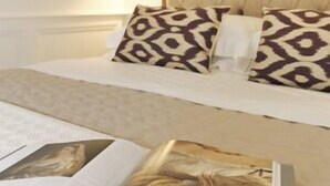 A neatly made bed with patterned pillows, a book, and a lamp on the side. - SantaCroce Junior Luxury Suite (Firenze)