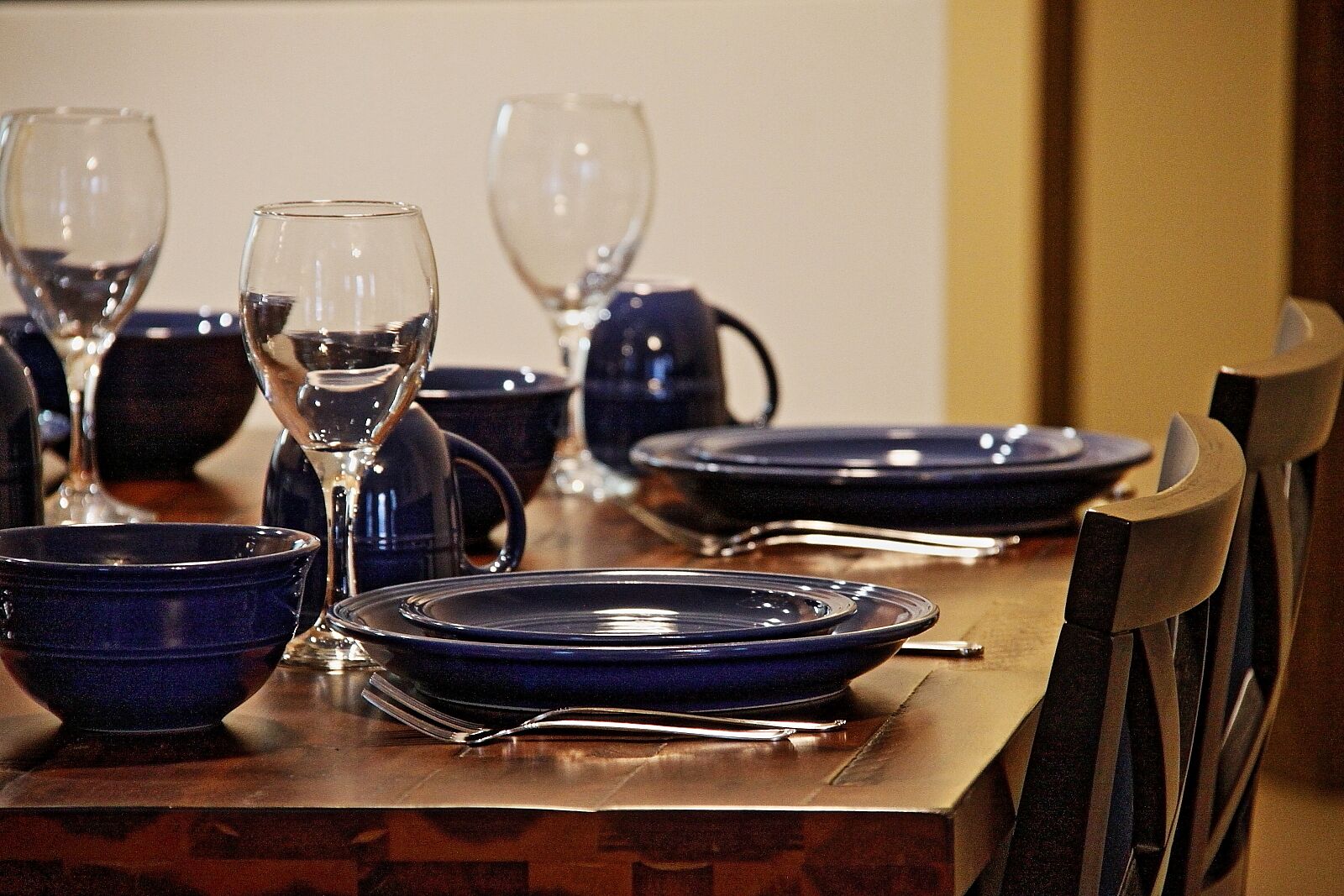 Een eettafel gedekt met blauwe borden, kommen en wijnglazen, omringd door stoelen.