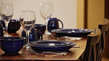 Een eettafel gedekt met blauwe borden, kommen en wijnglazen, omringd door stoelen.