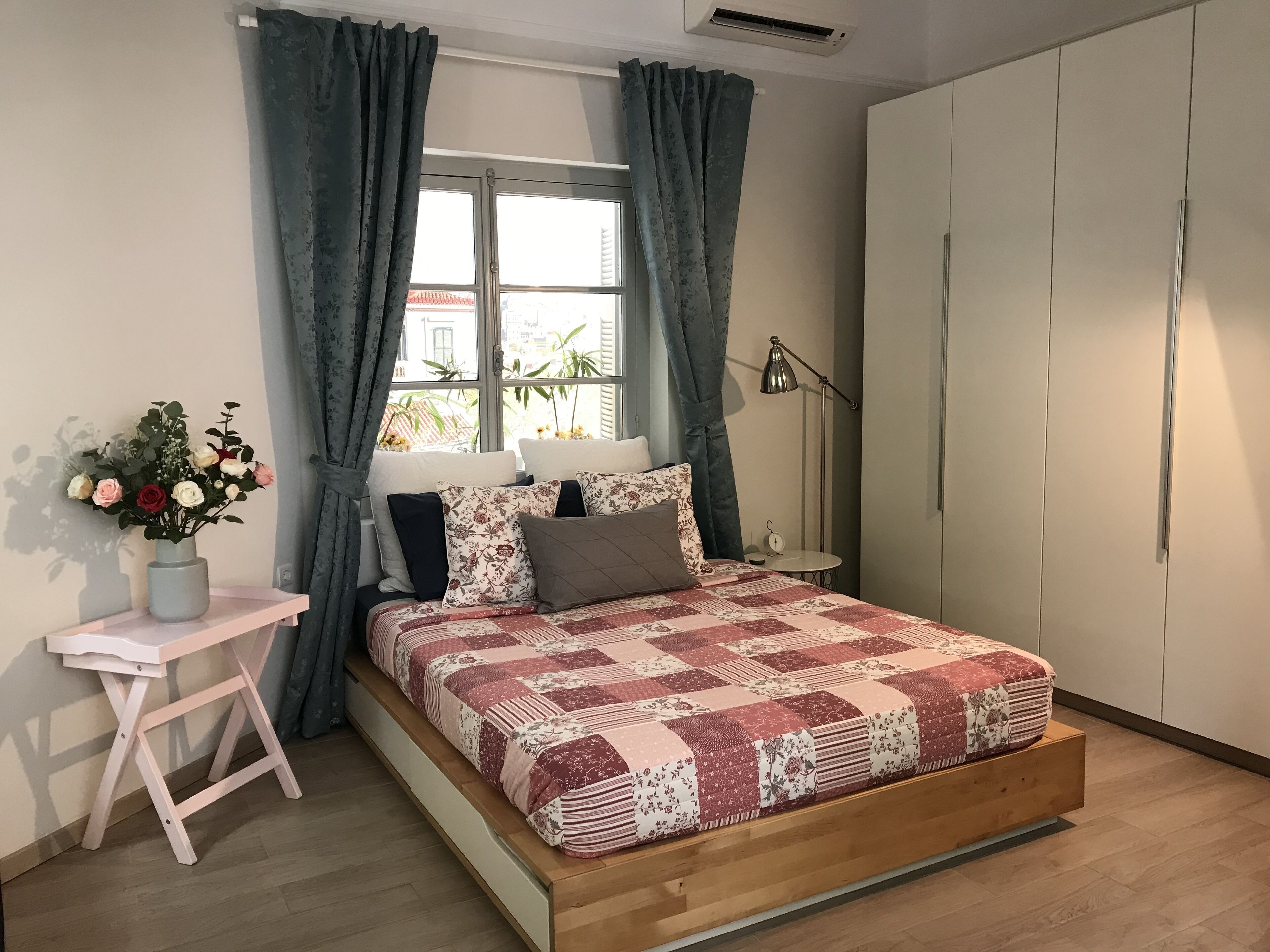 A bedroom with a wooden bed, a small desk, a vase of flowers, and a window with curtains.