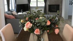 Un salon moderne comprenant une table à manger, un canapé, un téléviseur, une cheminée et un vase de fleurs.