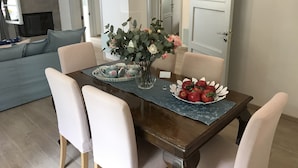 Une table à manger agrémentée d’un centre de table floral, un plateau avec des tasses à thé et un saladier rempli de fruits.