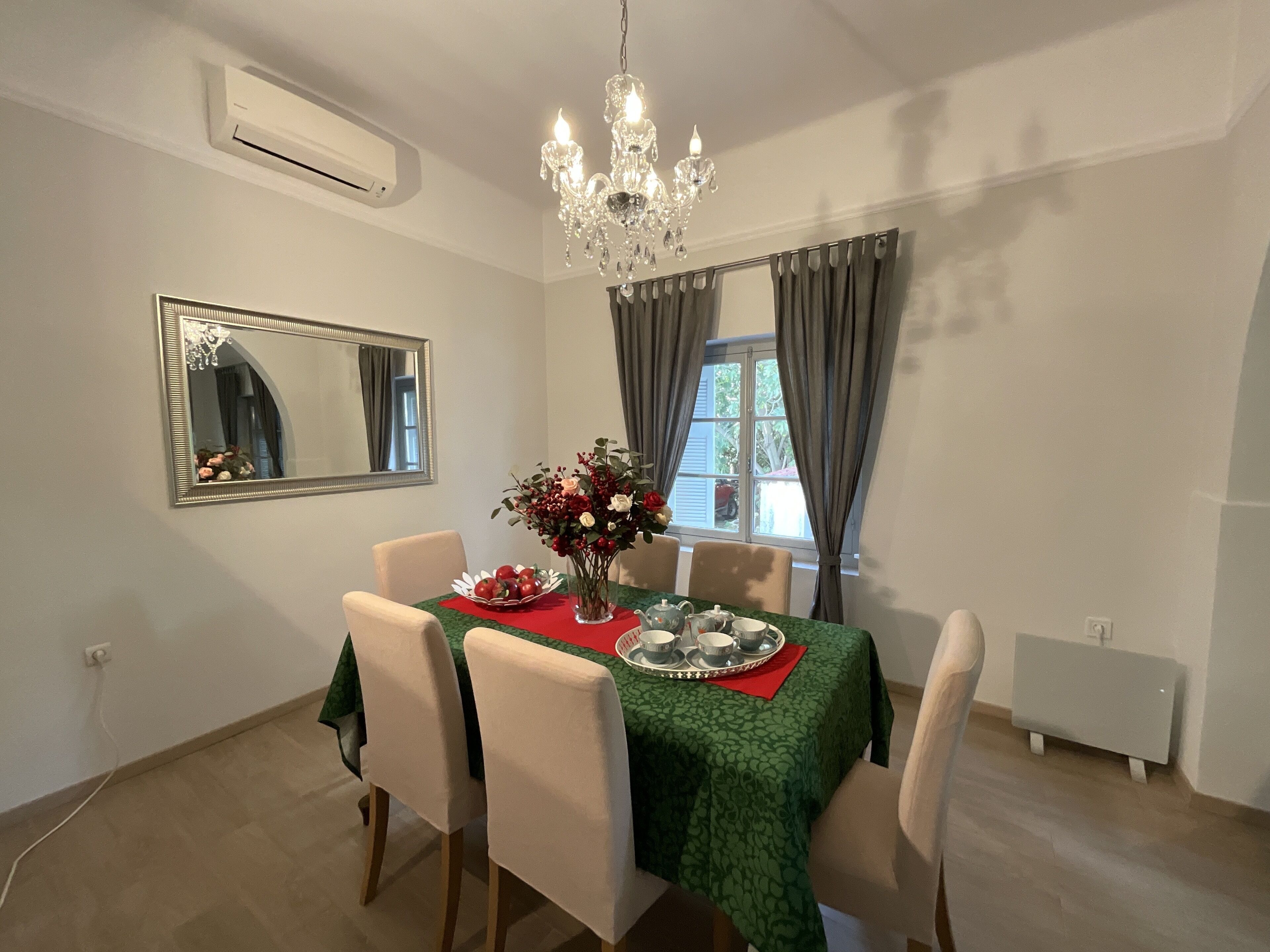 A dining area with a table set for four, a chandelier, a mirror, and a window with curtains.