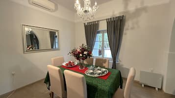 A dining area with a table set for four, a chandelier, a mirror, and a window with curtains.