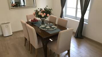 A dining area with a wooden table, six chairs, a vase of flowers, and a tray with teacups and apples.