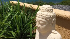 Una estatua de Buda cerca de una playa arenosa, con un cielo azul despejado y el océano al fondo.